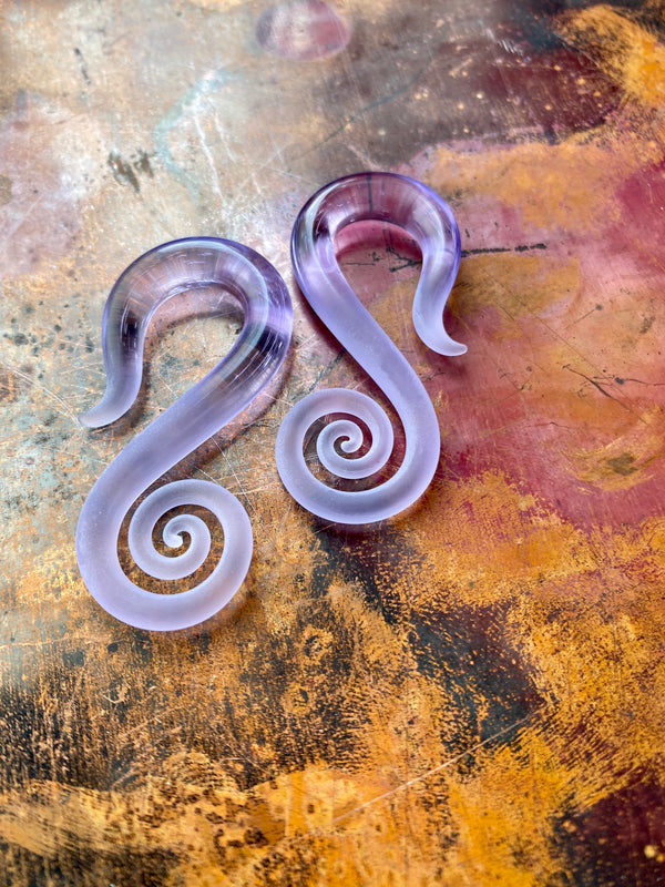 This is a pair of Pyrex or Borosilicate glass hangers in 2G. This image shows a pair of glass gauges in Purple Rain with a seaglass finish on the bottom half. This is a mid-size example of how this made-to-order pair will look when you get it. This purple glass is a fan favorite and a signature style of Glassheart body jewelry. Each pair is made to order and handcrafted by the artist in Eugene, OR.